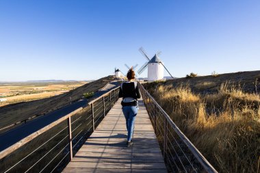 Mancha 'nın tarihi yel değirmenlerini berrak mavi gökyüzünün altında keşfeden bir kadın.