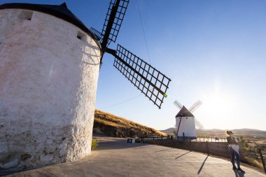 Geleneksel yel değirmenlerinin yanında duran bir kadın La Mancha manzarasına tepeden bakıyor.