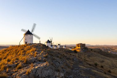 İspanya 'nın La Mancha şehrinde altın saat boyunca bir tepenin üzerinde duran yel değirmenleri ve şato