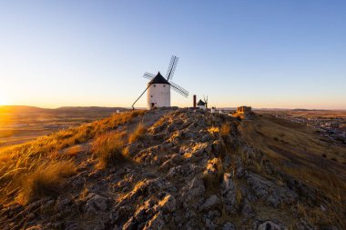Günbatımında İspanya 'nın Consuegra kentindeki kayalık bir tepede duran geleneksel İspanyol yel değirmenleri