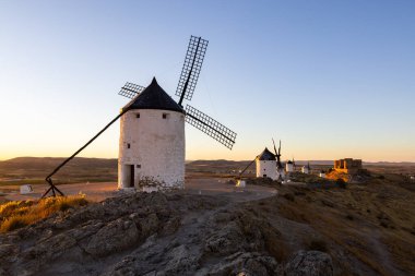 Antik yel değirmenleri ve İspanya 'nın La Mancha şehrinde altın saatinde aydınlatan bir kale.