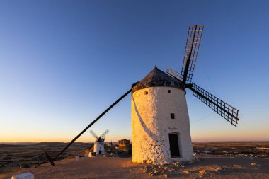 İspanya, Consuegra 'da altın saat gün batımında beyazlatılmış yel değirmenleri bir tepede duruyor.