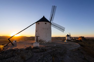 Gün batımında tepede duran yel değirmenleri ikonik bir La Mancha manzarası yaratıyor.