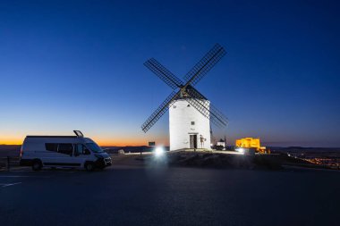 Ufuk alacakaranlıkta parlayan Consuegra yel değirmenine park etmiş bir karavan.