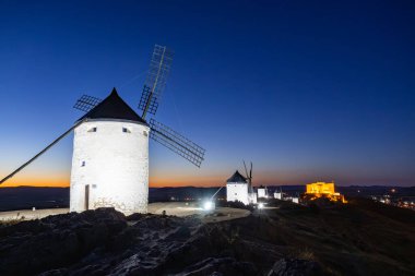 Consuegra yel değirmenleri ve Muela Şatosu Castilla La Mancha 'da alacakaranlıkta manzarayı aydınlatıyor.