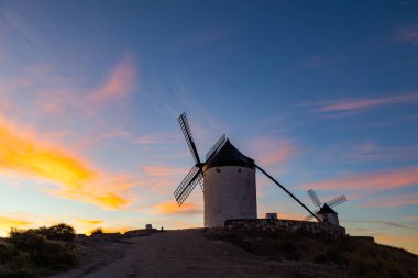 La Mancha 'da dramatik bir günbatımına karşı bir tepenin üzerinde duran tarihi yel değirmenleri.