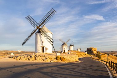 Geleneksel İspanyol yel değirmenleri ve güneş doğarken tepede duran antik bir şato.