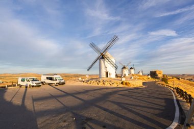 İspanya 'nın Consuegra kentindeki tarihi yel değirmenlerine bakan bir yola park etmiş karavan.