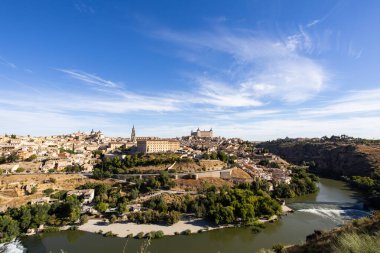 Toledo şehrinin tarihi binaları ve açık mavi gökyüzünün altındaki Tagus nehri.