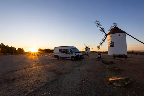 Altın saat boyunca bir tepenin tepesinde geleneksel yel değirmenlerinin yanına park edilmiş bir karavan.