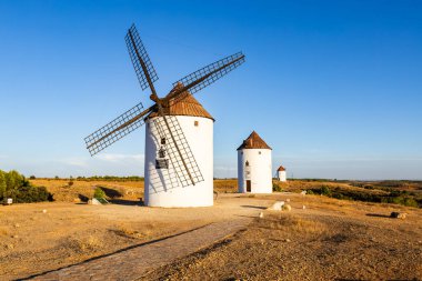 İspanya 'da açık mavi gökyüzünün altında kuru bir Kastilya manzarası üzerinde duran tarihi rüzgar değirmenleri