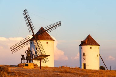 Beyaz yel değirmenleri ve gün batımında tepede duran Don Kişot heykeli.