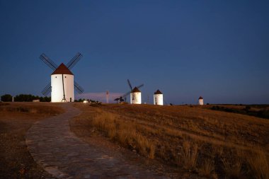 Mota del Cuervo 'daki kuru tepelerde duran yel değirmenleri koyu mavi bir alacakaranlık gökyüzüyle