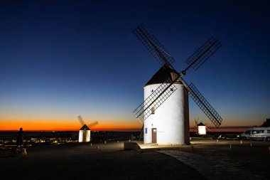 Akşam karanlığında turuncu ve mavi bir gökyüzünün altında duran İspanyol yel değirmenleri.
