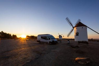 İspanya, Mota del Cuervo 'daki eski yel değirmenlerine bakan bir karavan güzel bir gündoğumu sırasında park edilmiş.