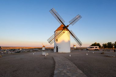 Tarihsel yel değirmenleri, Mota del Cuervo kasabasında alacakaranlıkta altın ışığı yansıtıyor.