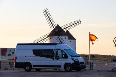 İspanya 'nın Mota del Cuervo kentinde seyahat ve macerayı sembolize eden İspanyol bayrağı ve yel değirmenlerinin yanına park etmiş bir karavan.
