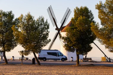 Gün batımında tarihi bir rüzgar değirmeninin yanına park etmiş bir karavan seyahat ve özgürlüğü gösteriyor.