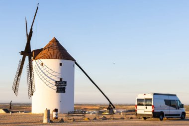 Geleneksel İspanyol yel değirmeni La Mancha 'da park etmiş bir karavanla bir tepede duruyor.