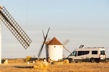 Gün batımında Mancha 'nın kuru manzarasında tarihi yel değirmenlerinin yakınına park edilmiş bir karavan.