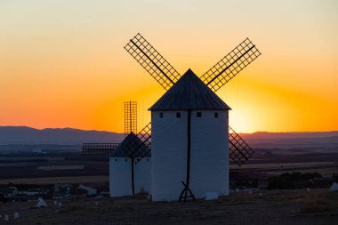 Geleneksel İspanyol yel değirmenleri La Mancha 'da alacakaranlıkta canlı turuncu bir gökyüzüne karşı duruyor.