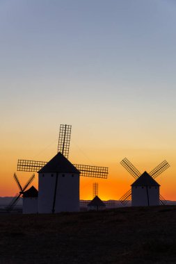 Tepede duran tarihi yel değirmenleri dramatik bir La Mancha gün batımına karşı bir siluet oluşturuyor.