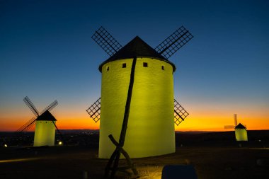 La Mancha 'da geleneksel yel değirmenleri alacakaranlıkta renkli bir gökyüzünün altında bir tepenin üzerinde duruyor.