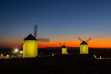 Geleneksel İspanyol yel değirmenleri canlı bir günbatımı gökyüzüne karşı tarihi bir tepenin üzerinde duruyorlar.