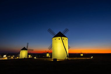 İspanya, Campo de Criptana 'da bir tepede duran yel değirmenleri, alacakaranlıkta turuncu bir günbatımı parıltısıyla