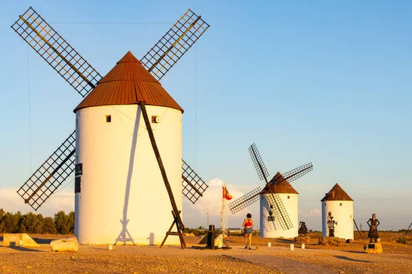 İspanya, La Mancha 'da açık bir gökyüzü altında beyaz yel değirmenlerini izleyen bir kadın.