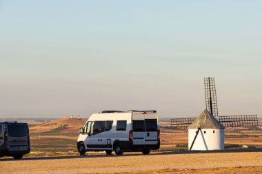 Kamp aracı, Campo de Criptana 'da günbatımında tarihi bir yel değirmeninin yanında duruyor.