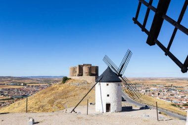 Geleneksel İspanyol yel değirmenleri ve bir kale açık mavi gökyüzünün altındaki Consuegra yamaçlarına hakim.