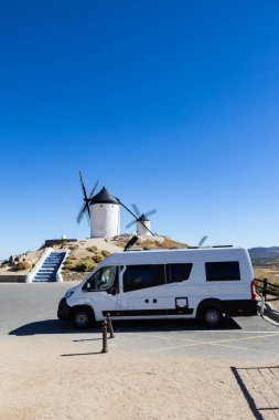 Güneşli bir günde Consuegra, İspanya 'da tarihi yel değirmenleriyle park edilmiş bir karavan.