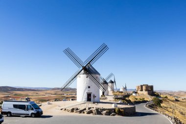 Consuegra 'da açık mavi gökyüzünün altında duran yel değirmenleri ve tarihi bir kale.