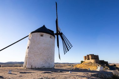 Geleneksel Don Kişot tarzı yel değirmeni açık mavi gökyüzünün altında taş bir şatosu var.