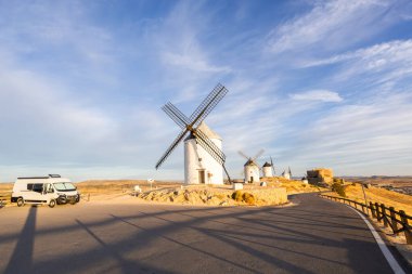 Yolda park etmiş bir karavan, beyaz yel değirmenlerinin ve mavi gökyüzünün altında eski bir şatonun tadını çıkarıyor.