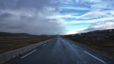 Islak bir yolda giden araba çorak bir arazide bulutlu bir gökyüzünün altındaki Kuzey Burnu 'na doğru gidiyor.