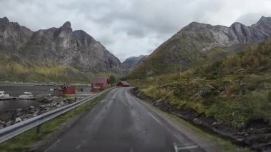 Bakış açısı bulutlu bir sonbahar gününde Norveç fiyortlarında manzaralı bir yolda araba sürmektir.