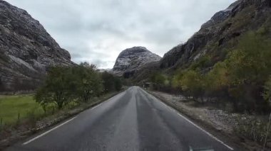 POV, Norveç 'te bulutlu bir günde, kayalık bir vadiden geçen asfalt bir yolda karavanı sürüyor.