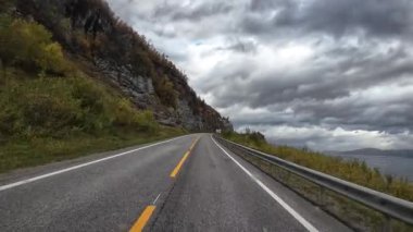 Bulutlu bir sonbahar gününde Norveç fiyortu boyunca giden bir karavanın manzarası.