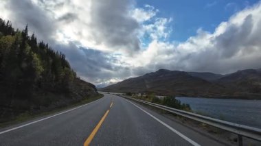 Perspektif, dramatik bulutlu bir gökyüzü altında dağlarla çarpıcı bir Norveç fiyordu boyunca araba sürüyor.