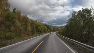 Bulutlu bir gökyüzünün altında sonbahar renkleriyle çarpıcı bir Norveç fiyort yolu boyunca karavan yolculuğu