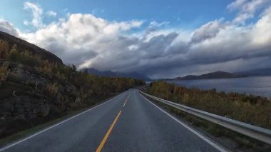 Norveç 'in kuzeyinde sonbahar boyunca bir fiyort ile birlikte pitoresk bir yolda araba süren bakış açısı