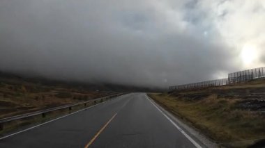 Norveç kırsalında ıslak asfalt yol boyunca giden bir kampçının bakış açısı