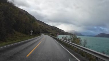 Norveç 'te güzel bir fiyordun yanındaki ıslak asfalt yolda çekilen fotoğraf.