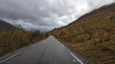 Bulutlu bir sonbahar gününde Senja adasında ıslak bir asfalt yolda bir karavanı sürmek.