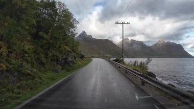 Senja 'da bulutlu bir günde, kıyı boyunca uzanan ıslak asfalt bir yolda uçan çarpıcı bir araç.