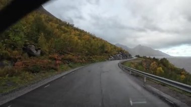 Norveç 'in Senja kentindeki bir fiyort boyunca dolambaçlı bir sahil yolunda yağmurlu bir günde çekilen görüntüler.