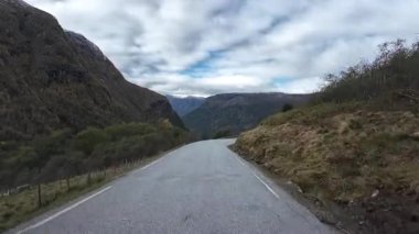 Bakış açısı, sonbaharda Norveç manzarası boyunca manzaralı bir dağ yolunda ilerliyor.