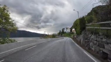 Norveç 'te bulutlu bir günde, bir fiyordun yanında dar bir kıyı yolu boyunca araba sürerken çekilmiş bir bakış açısı